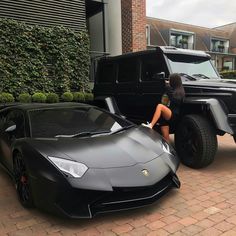 a woman sitting on the hood of a black sports car next to a lambino