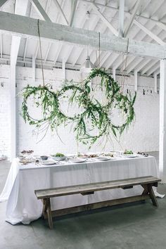 the table is set up with white linens and greenery hanging from the ceiling