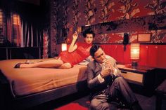 a man and woman sitting on a bed in the middle of a room with red walls