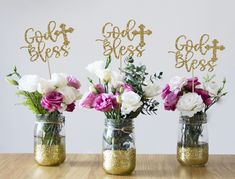 three mason jars filled with flowers and gold glittered cake toppers that spell out god's blessing