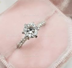 an engagement ring is sitting on top of a pink velvet bag with the diamond set in it's center