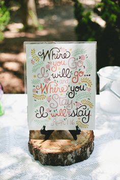 a sign sitting on top of a wooden stump next to a table with white cloth