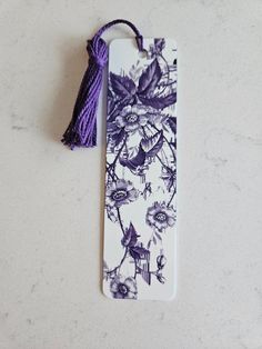 a purple and white bookmark with an image of flowers on it, hanging from a tassel