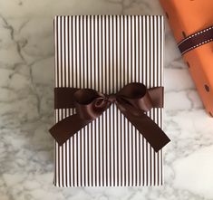 a gift wrapped in chocolate paper with a brown bow on the top, sitting on a marble surface