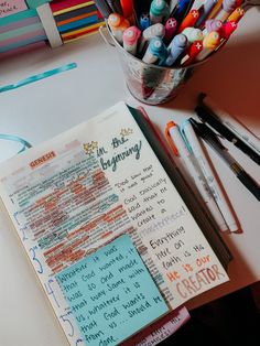 an open notebook sitting on top of a table filled with markers and pens