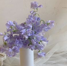 a white vase filled with purple flowers on top of a table