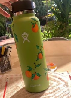 a person is holding the lid on a green water bottle with oranges painted on it