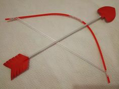 a red bow and arrow made out of paper on top of a white sheeted surface