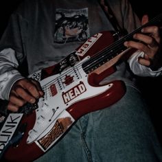 a man holding a red and white guitar in his right hand with the word head on it