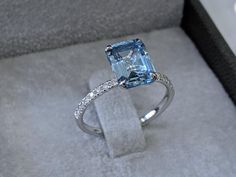 a ring with an aqua blue topazte surrounded by white diamonds in a box