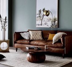 a living room with brown leather furniture and paintings on the wall above it's windows