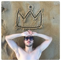 a shirtless man is laying in the sand with his hands on his head and wearing sunglasses