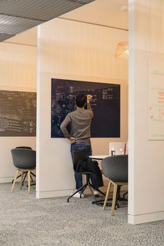 a man is writing on a blackboard in an office with chairs and desks