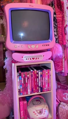 a pink toy tv sitting on top of a book shelf filled with books and toys