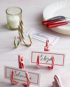 candy cane place card holders with name tags on them sitting on a table next to plates and candles