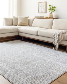 a living room with a large white couch and rug on top of the wooden floor