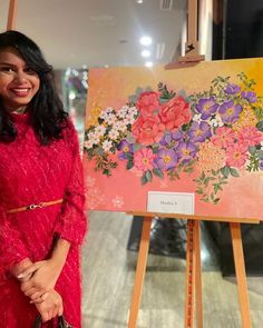 a woman standing next to an easel with flowers painted on it and holding a purse