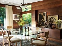 a glass dining table surrounded by chairs in a room with wood paneling and windows