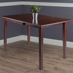 a small wooden table with a plant in the middle on top of it, against a gray wall