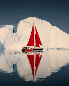 a red sailboat in front of an iceberg with water reflections on the surface