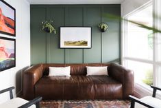 a brown leather couch sitting in a living room next to two pictures on the wall