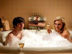 a man and woman sitting in a bathtub with bubbles on the side holding wine glasses