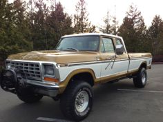 a tan and white pickup truck parked in a parking lot next to some pine trees