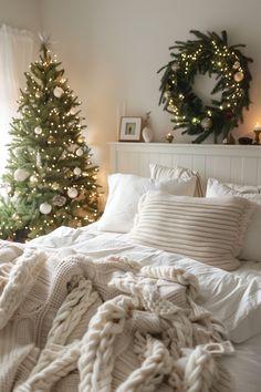 a white bed topped with pillows and blankets next to a christmas tree