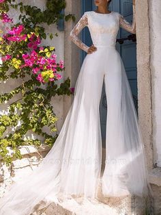 a woman standing in front of a doorway wearing a white wedding dress with sheer sleeves