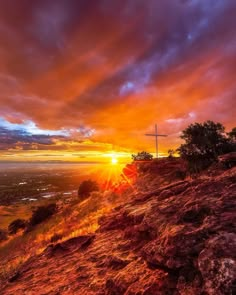 the sun is setting on top of a hill with a cross in the foreground