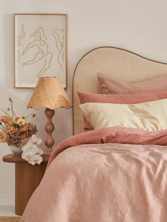 a bed with pink linens and pillows in a white room next to a lamp