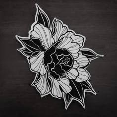 a black and white flower with leaves on it's back side, sitting on a wooden surface