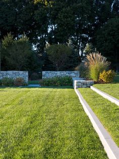 a large grassy yard with stone wall and trees in the background