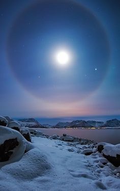 an image of the moon in the sky over some snow covered rocks and water with mountains in the background