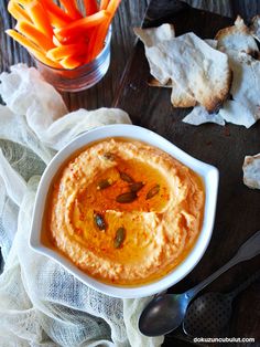 a bowl filled with hummus and carrots on top of a table next to bread