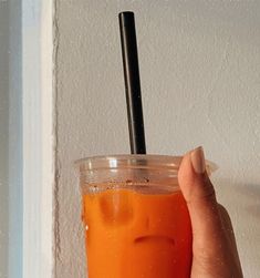 a hand holding an orange drink with a straw in it's cup and the lid partially closed