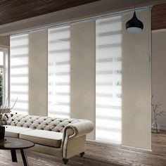 a living room filled with furniture and windows covered in white blinds next to a coffee table