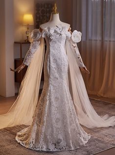 a white wedding dress with long sleeves and flowers on the shoulder, is displayed in front of a mannequin