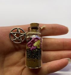 a hand holding a tiny bottle filled with flowers and an inverted pentagramil charm