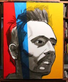 a painting of a man's face on a multicolored canvas with bookshelves in the background