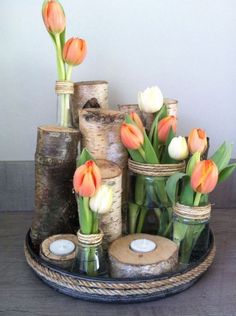 vases filled with flowers sitting on top of a wooden table next to logs and candles