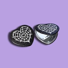 two black and white heart shaped compacts on a purple background with spider web design