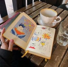 an open book sitting on top of a wooden table next to a cup of coffee