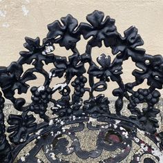 an iron bench with black flowers on it's back and sides, against a stucco wall