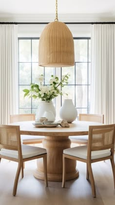 a dining room table with chairs and vases on it in front of a window