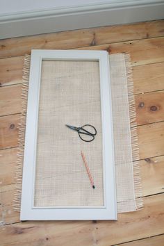 scissors are sitting on the floor in front of a white frame with a string attached to it