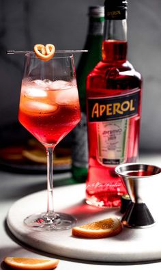 a bottle of aperol next to a glass filled with liquid and an orange slice