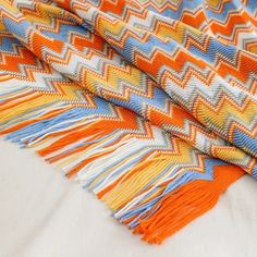 an orange, blue and white blanket laying on top of a bed next to pillows