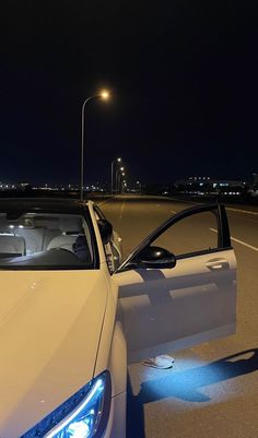 a white car is parked on the side of the road with its door open at night