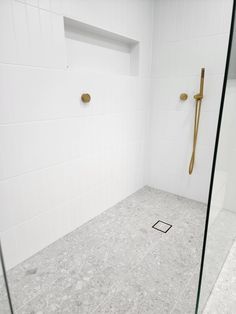 a white tiled bathroom with a glass shower stall and gold handles on the door handle